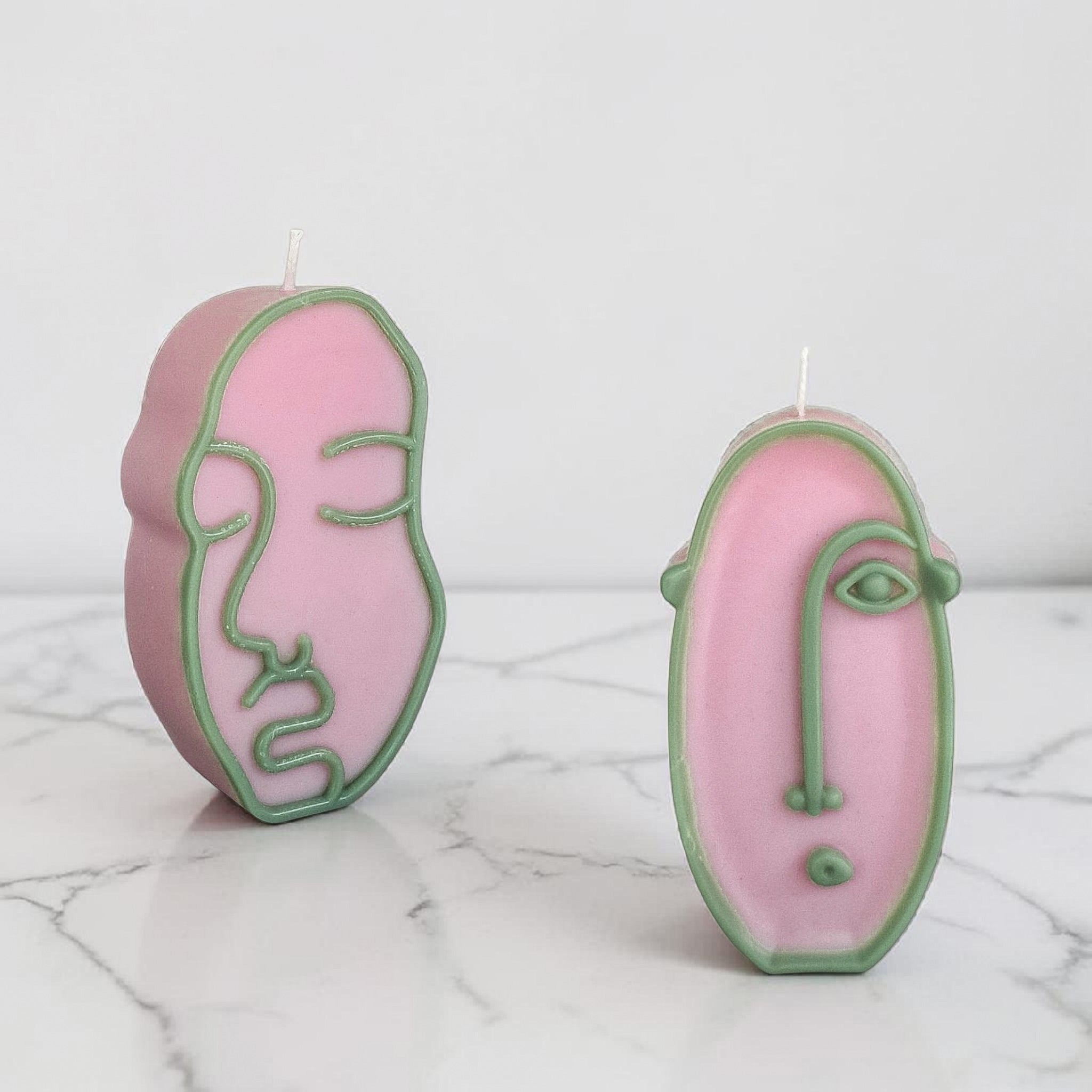 Two hand poured soy wax twisted pink candles on a marble surface
