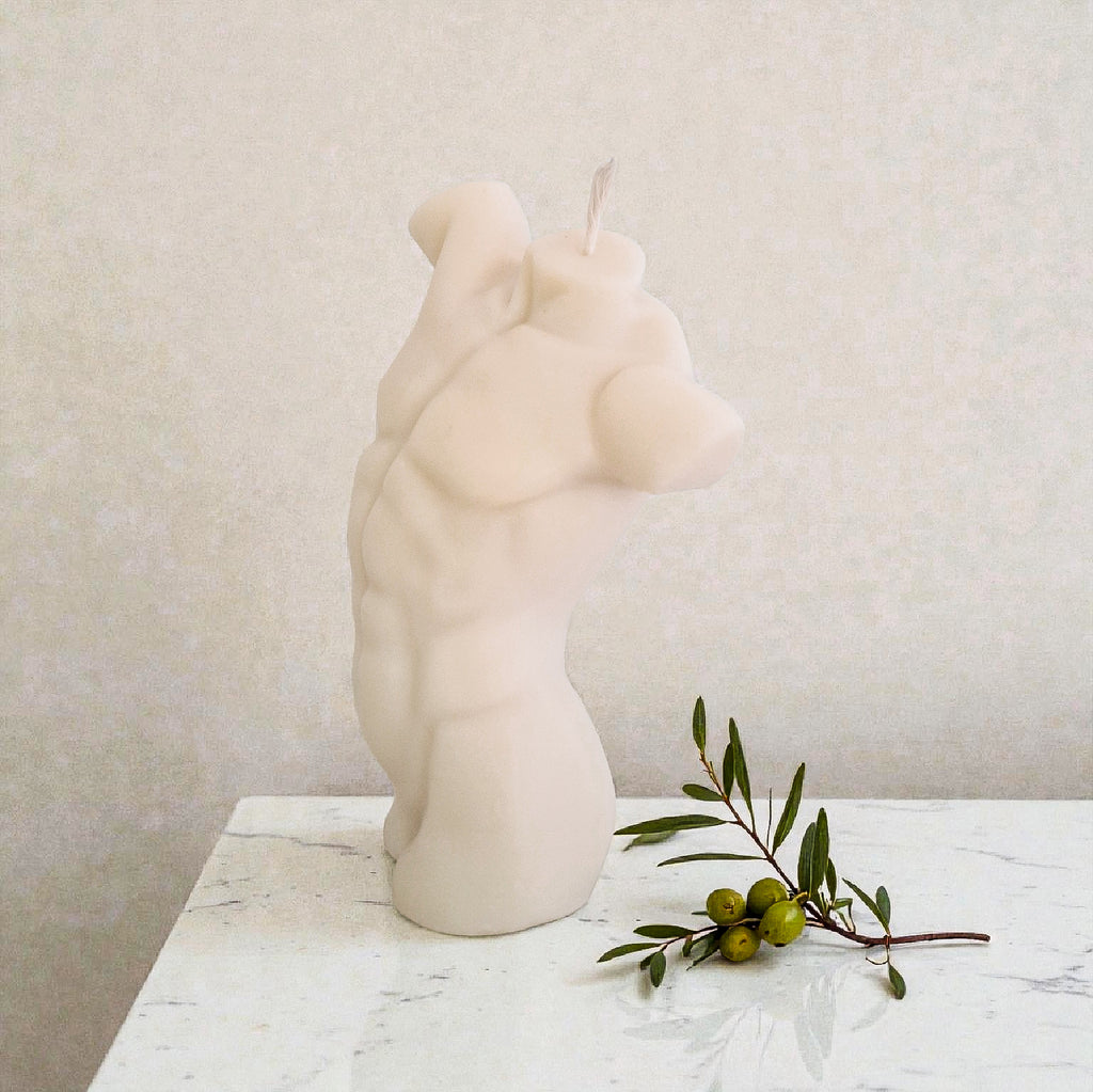 Candle shaped of a male torso on a marble surface with a branch of olives.