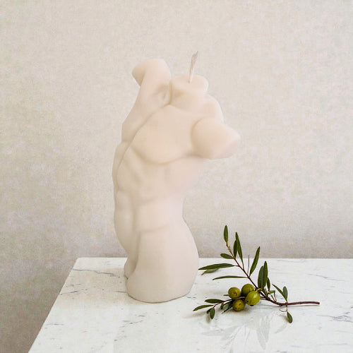 Candle shaped of a male torso on a marble surface with a branch of olives.