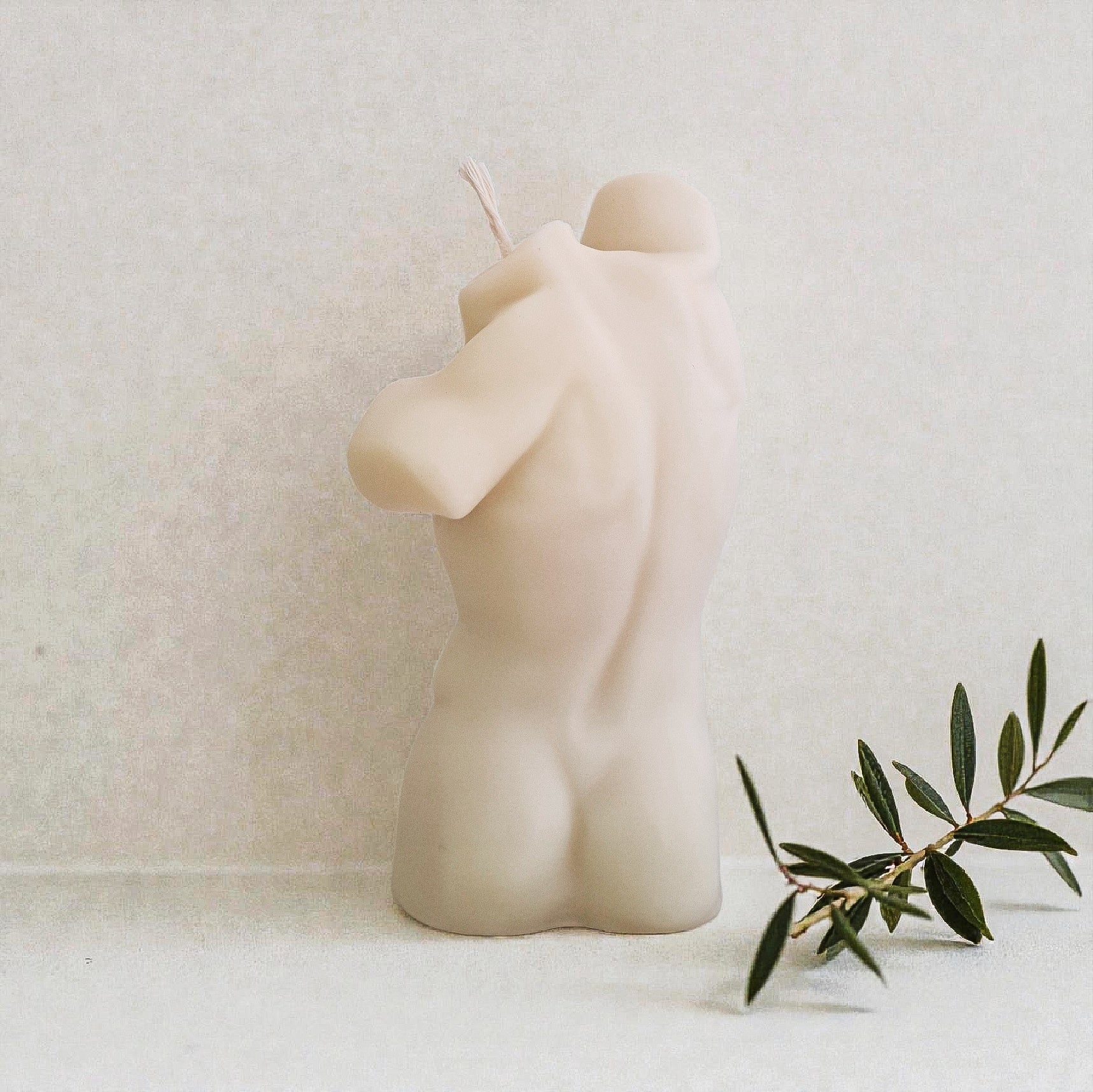 Ceramic sculpture of a nude figure on a white surface with a plant in the foreground