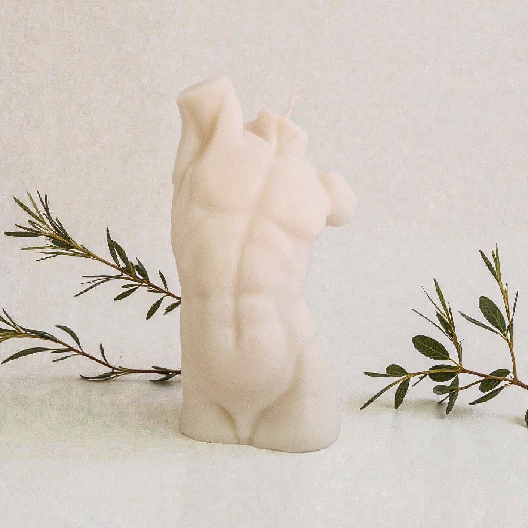 Candle shaped of a male torso on a marble surface with a branch of olives.