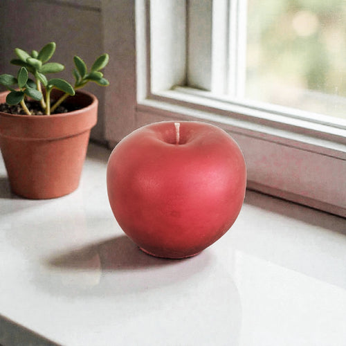 Red apple-shaped soy wax candle on a windowsill with a potted plant in the background