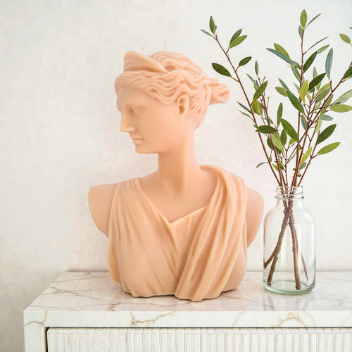 Artemis Bust soy wax sculpture e on a marble surface with a vase of greenery.