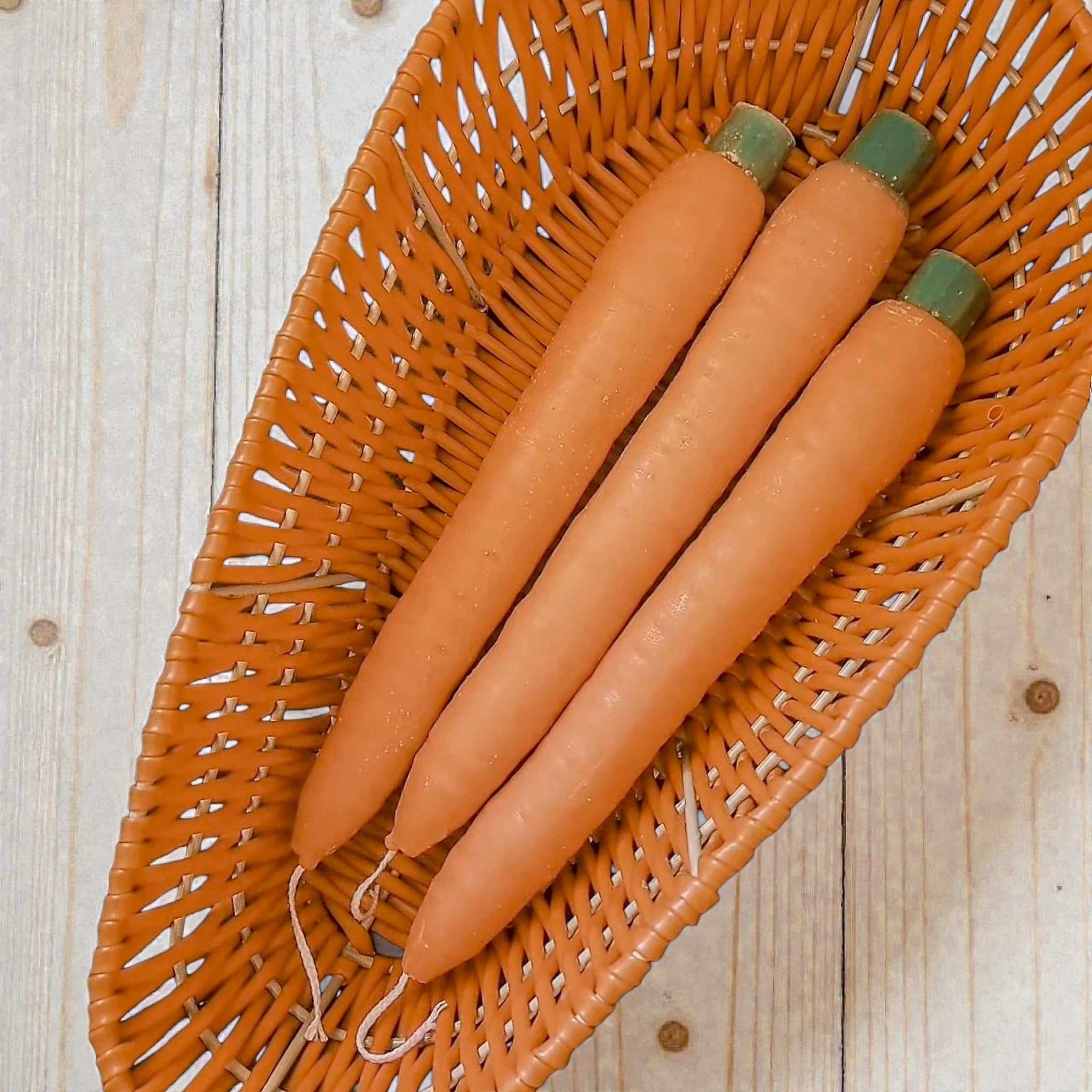 Three carrots with green tops in a wicker basket on a wooden surface