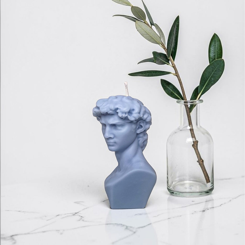 Blue bust soy wax candle and clear vase with olive branch on marble surface