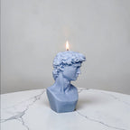 Blue bust-shaped soy wax candle with a lit wick on a marble surface.