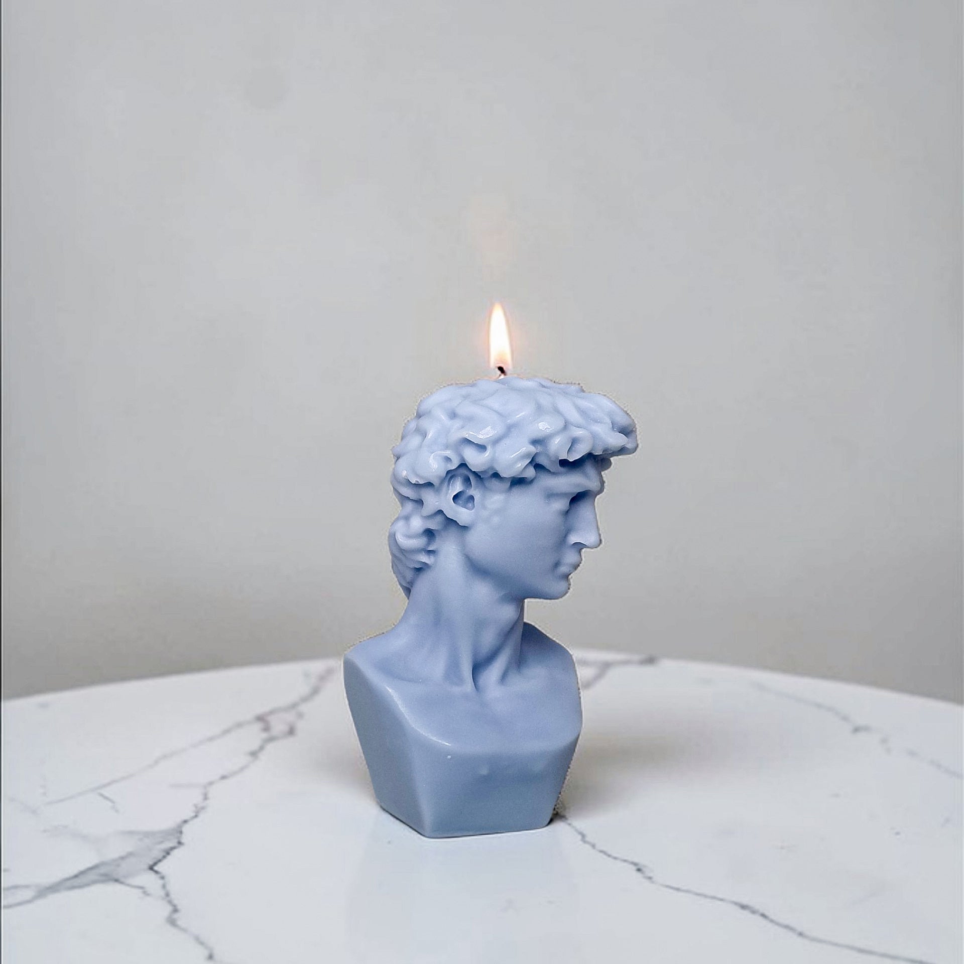 Blue bust-shaped soy wax candle with a lit wick on a marble surface.