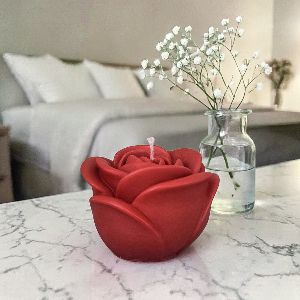 Hand poured soy wax red rose-shaped candle on a marble surface with a blurred bedroom background