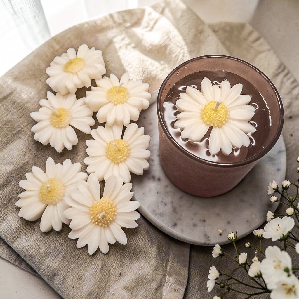 Daisy soy wax candle floating in a glass of water on a textured surface 