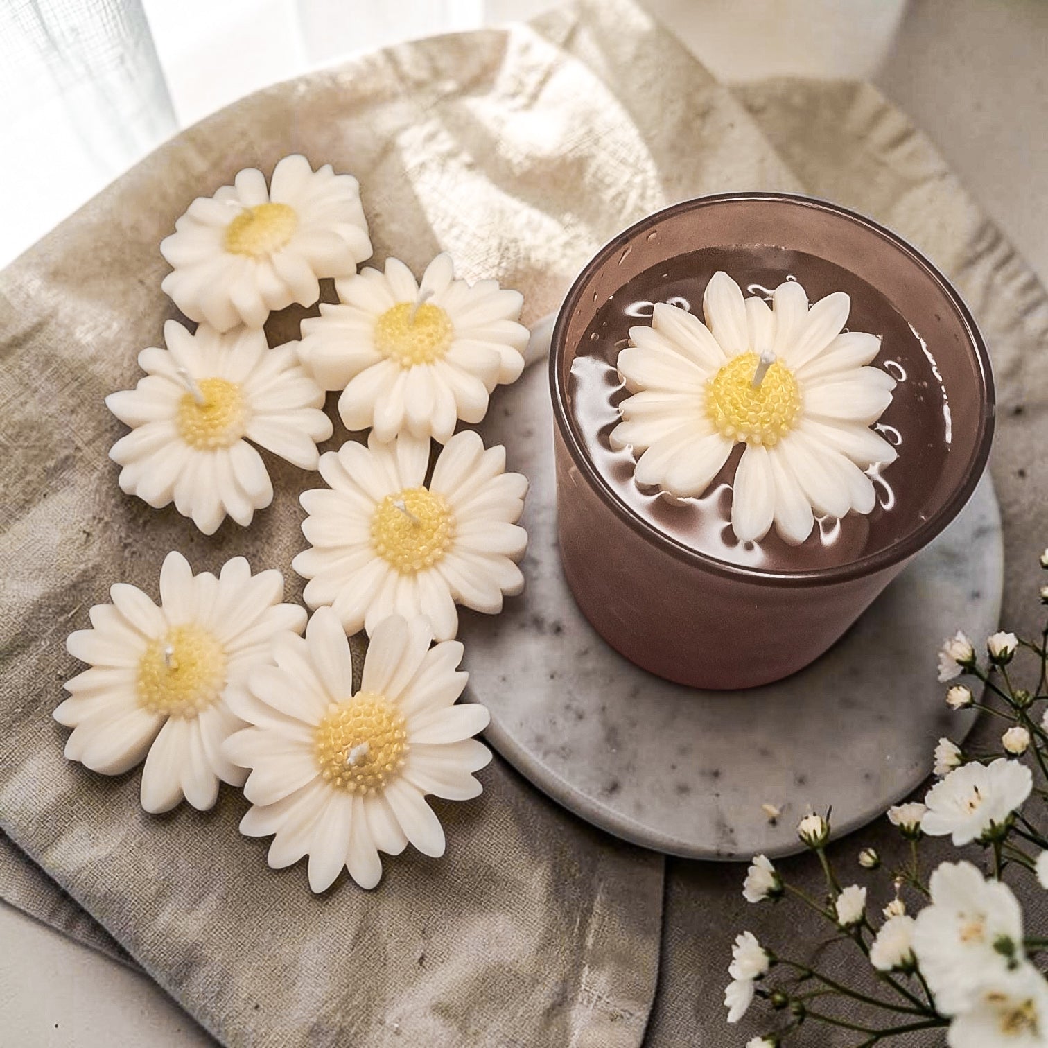 Daisy soy wax candle floating in a glass of water on a textured surface 