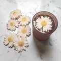 White daisy-shaped soy wax candles with yellow centres on a marble surface.