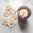 White daisy-shaped soy wax candles with yellow centres on a marble surface.