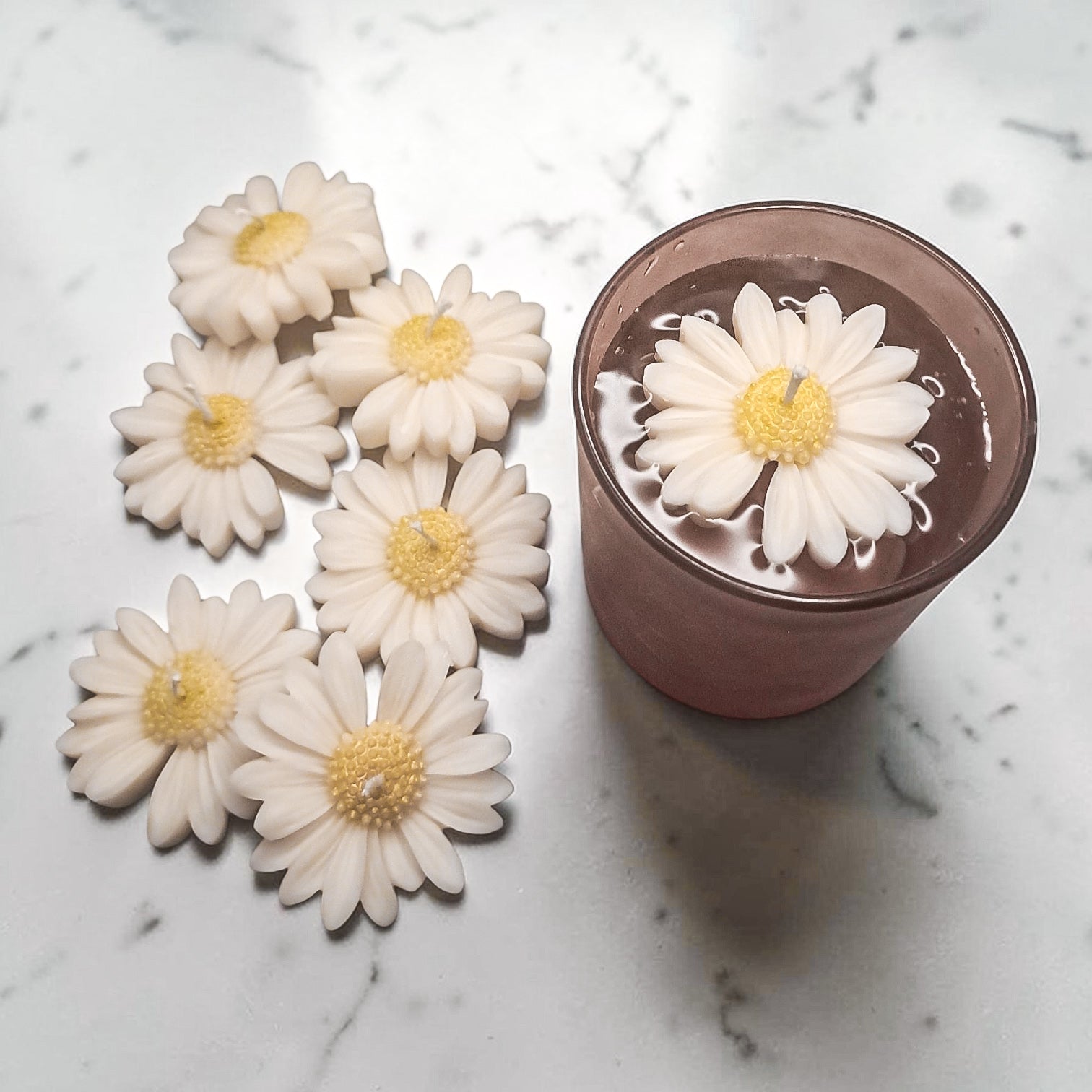 White daisy-shaped soy wax candles with yellow centres on a marble surface.