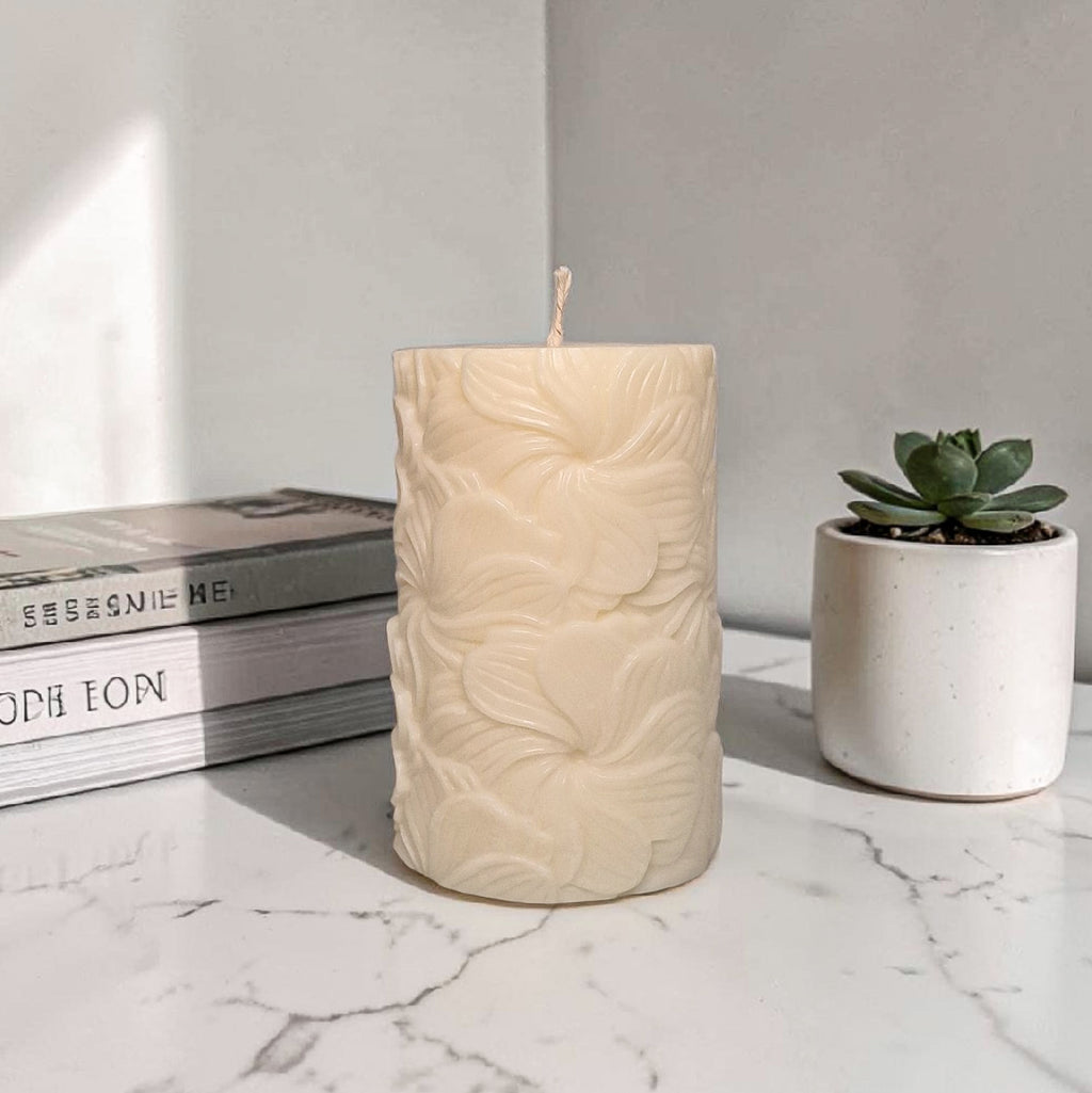 Beige textured floral pattern pillar soy wax candle on a marble surface with books and a succulent in the background