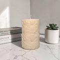 Beige textured floral pattern pillar soy wax candle on a marble surface with books and a succulent in the background