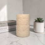 Beige textured floral pattern pillar soy wax candle on a marble surface with books and a succulent in the background