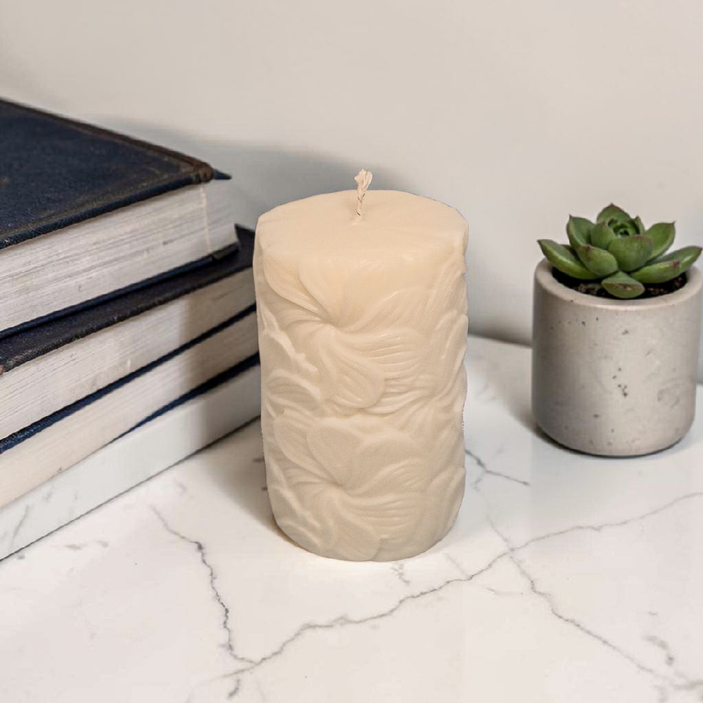 Beige textured floral pattern pillar soy wax candle on a marble surface with books and a succulent in the background