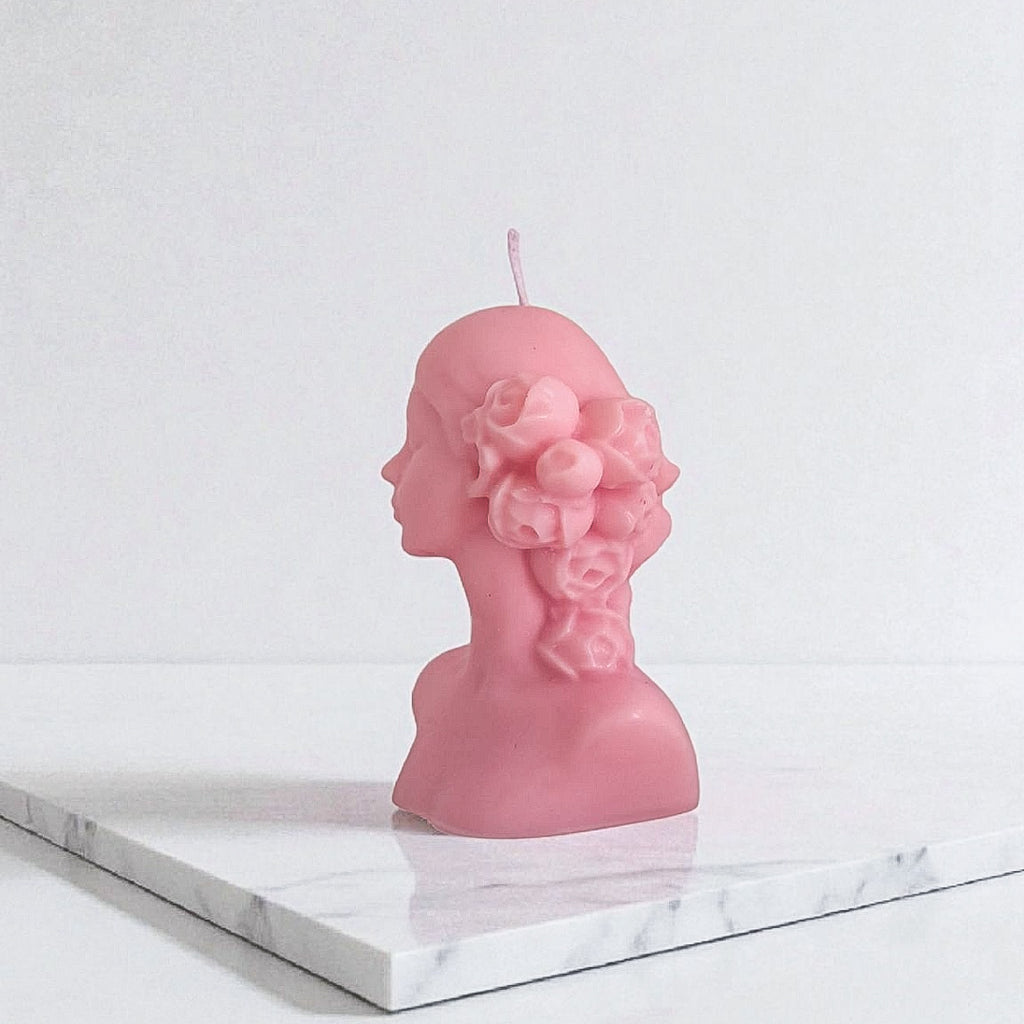 Pink bust-shaped candle on a marble surface with a white background