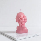Pink bust-shaped candle on a marble surface with a white background