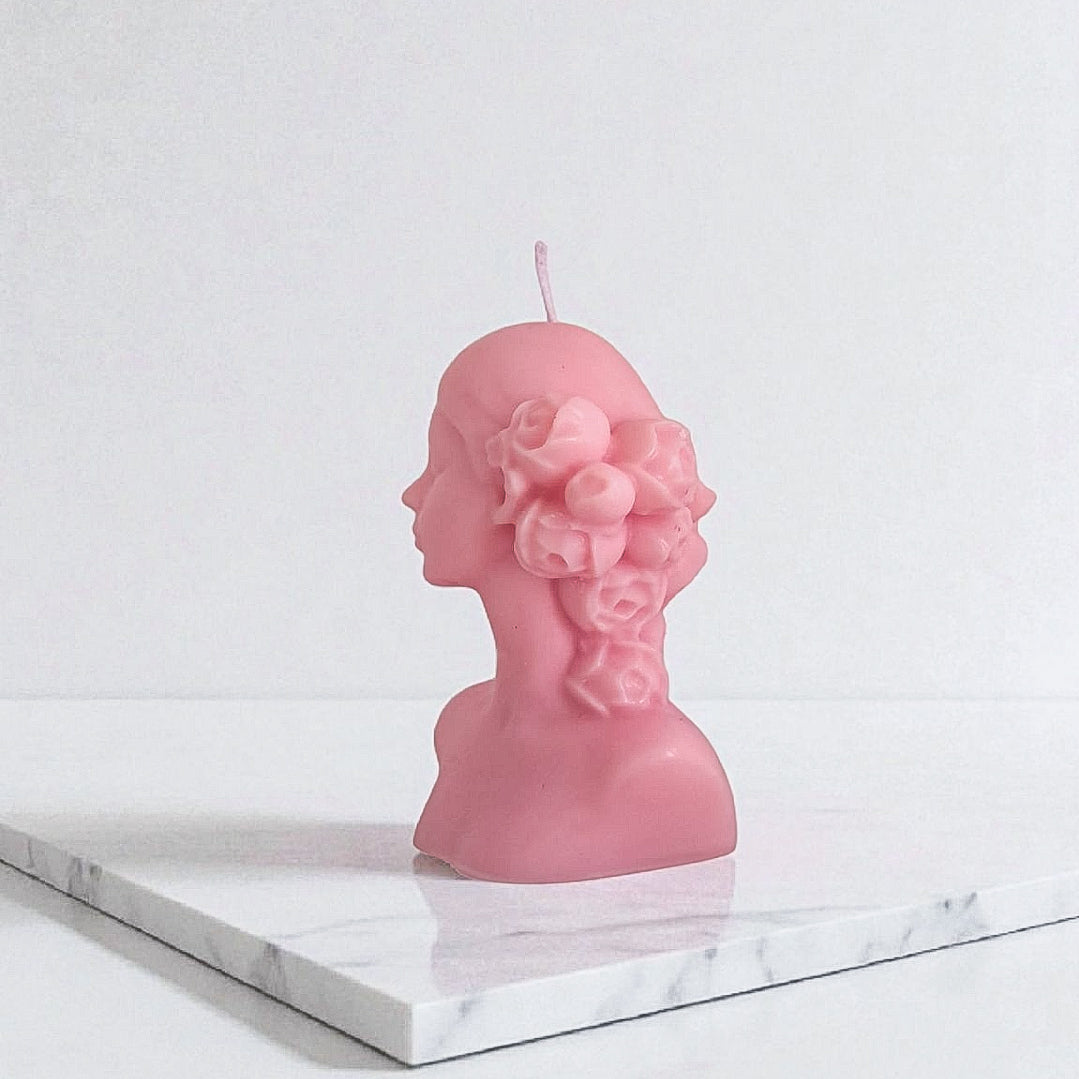 Pink bust-shaped candle on a marble surface with a white background