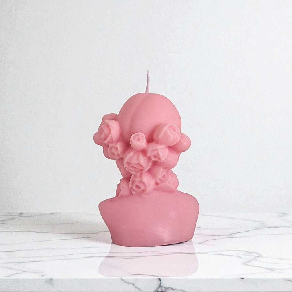 Pink bust-shaped candle on a marble surface with a white background
