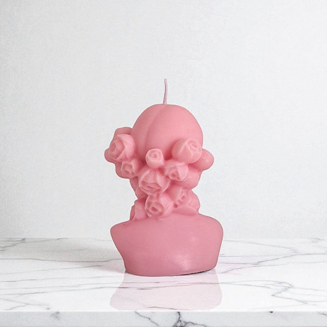 Pink bust-shaped candle on a marble surface with a white background