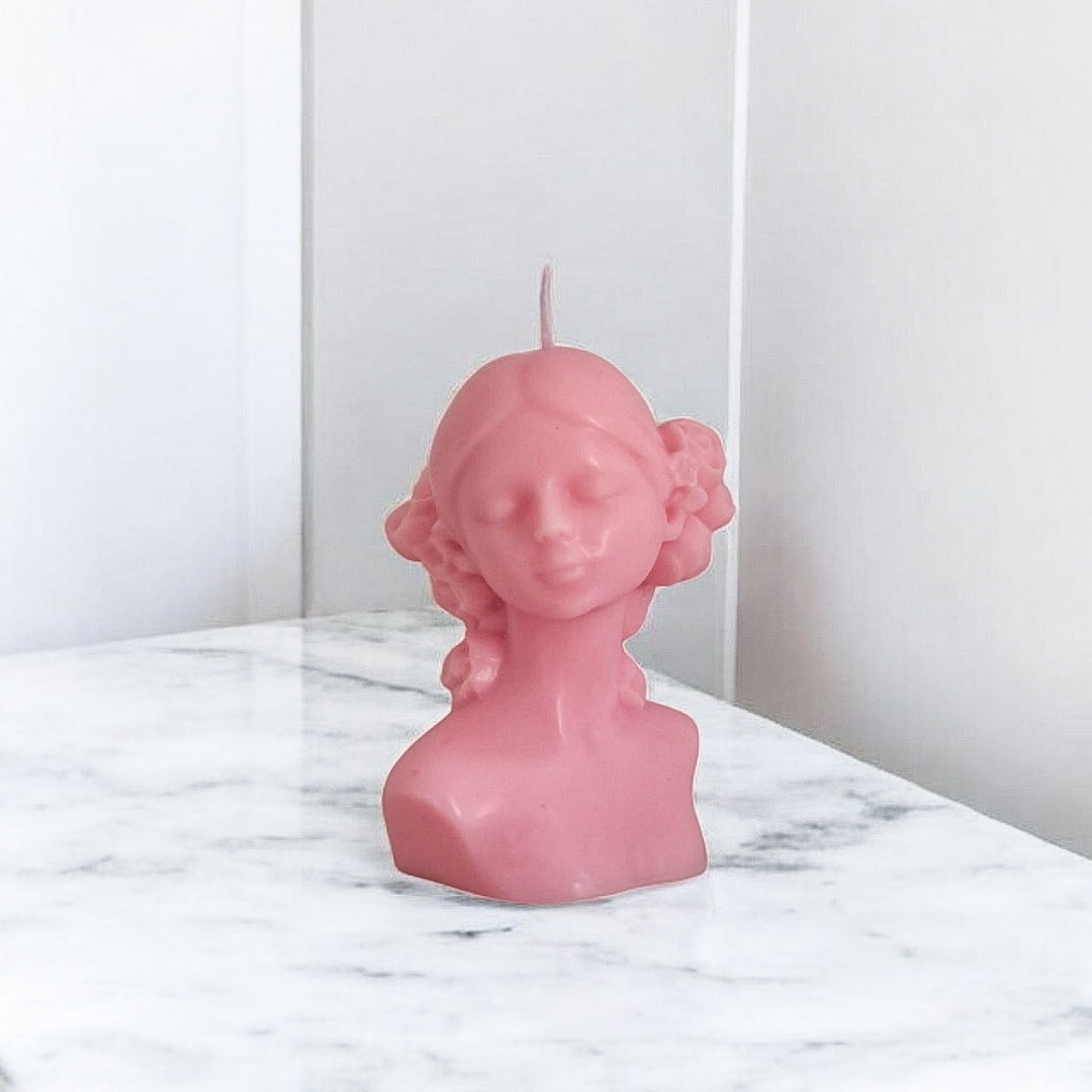 Pink bust-shaped candle on a marble surface with a white background