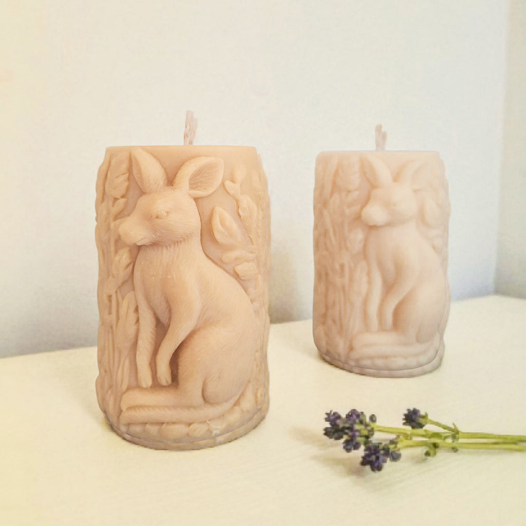 Two beige candles with animal carvings on a white surface with a light background