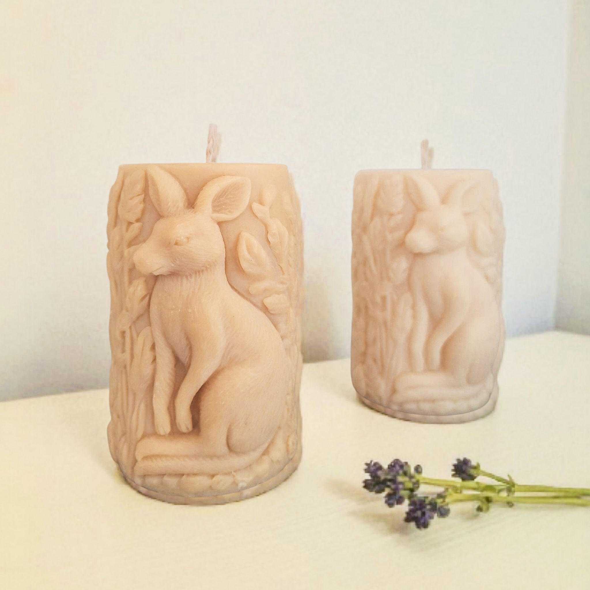 Two beige candles with animal carvings on a white surface with a light background