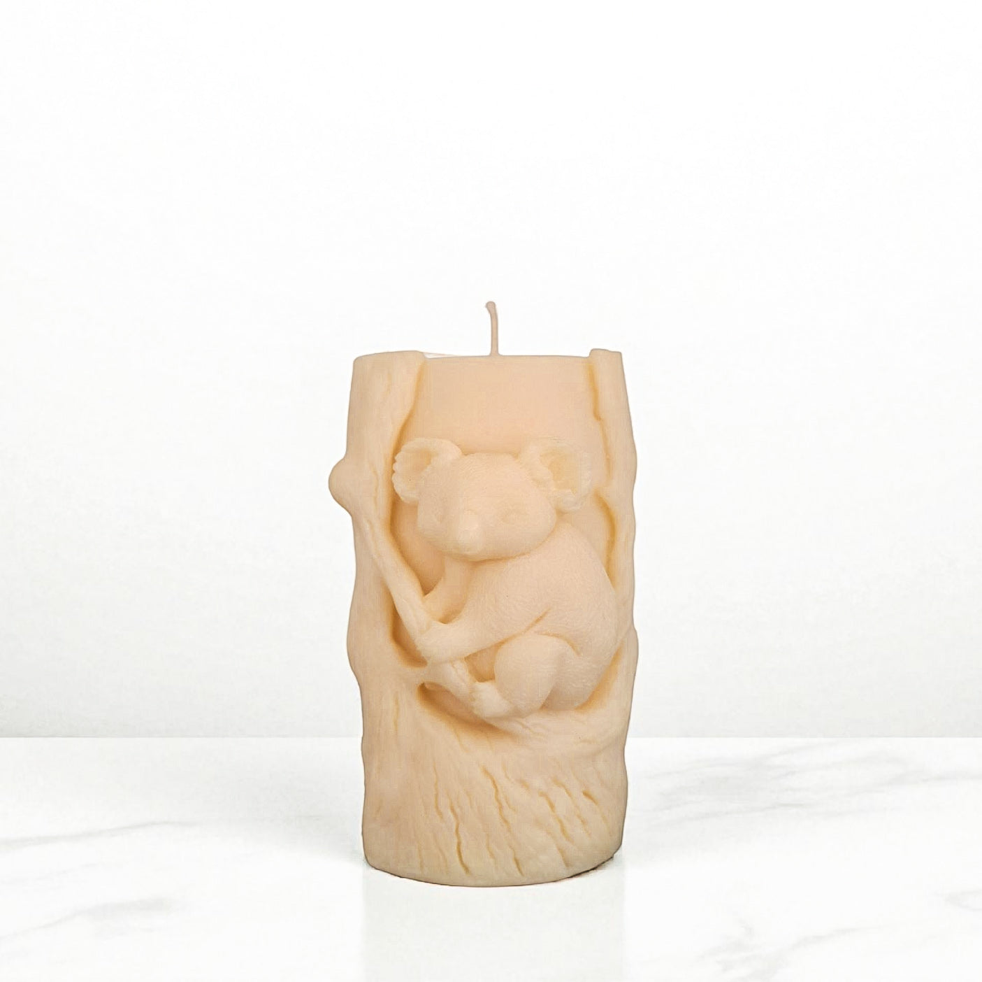 Soy wax candle shaped like a tree stump with a koala bear design on a white surface.