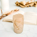 Beige soy wax candle shaped like a tree stump with a koala bear on a white surface with gold branches in the background