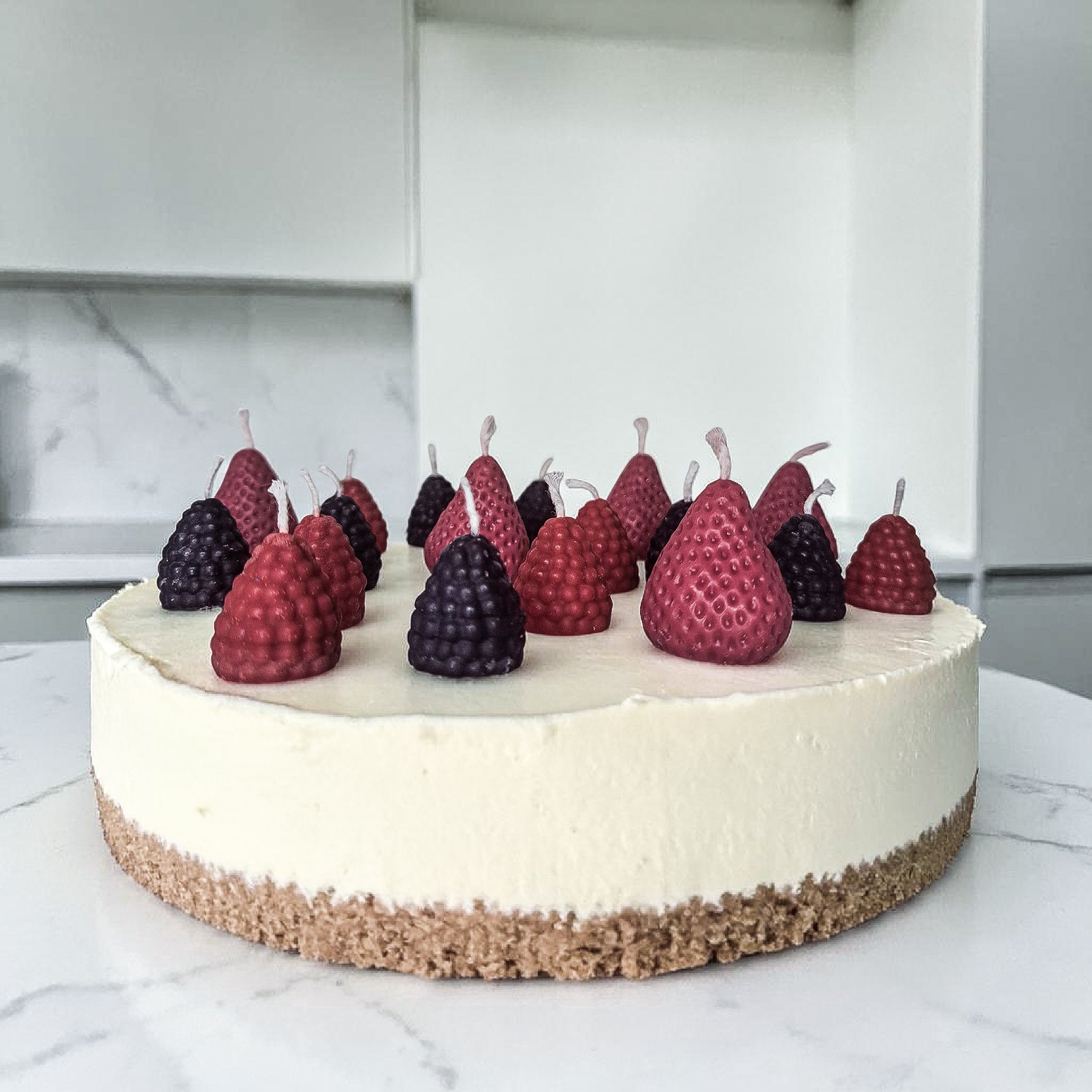 Decorative cake with hand poured strawberries, blackberries and raspberries soy wax birthday candles on a marble surface