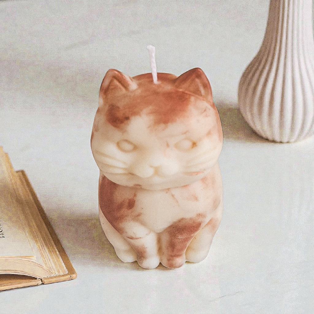 Sculptural cat-shaped soy pillar candle styled on marble surface with vase 