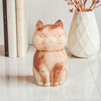 Sculptural cat-shaped soy pillar candle styled on marble surface with floral vase flowers