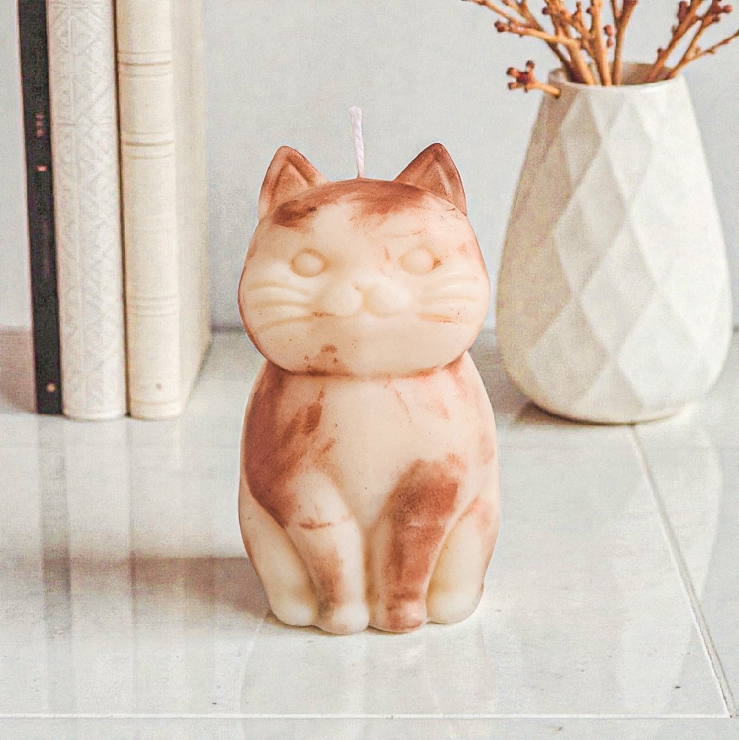 Sculptural cat-shaped soy pillar candle styled on marble surface with floral vase flowers