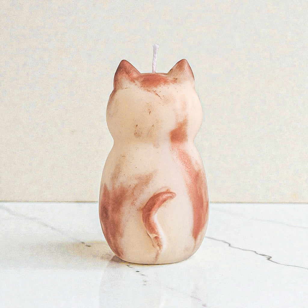 Sculptural cat-shaped soy pillar candle styled on marble surface with floral vase flowers