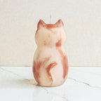 Sculptural cat-shaped soy pillar candle styled on marble surface with floral vase flowers