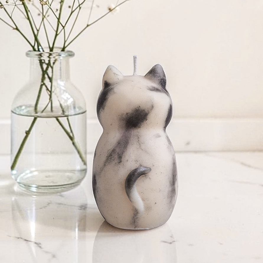 Sculptural cat-shaped soy pillar candle styled on marble surface with floral vase