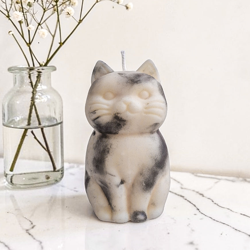 Sculptural cat-shaped soy pillar candle styled on marble surface with floral vase