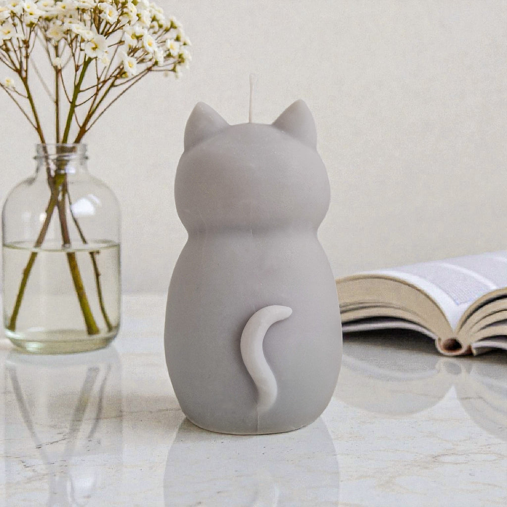 Sculptural cat-shaped soy pillar candle styled on marble surface with floral vase flowers and an open book in the background.