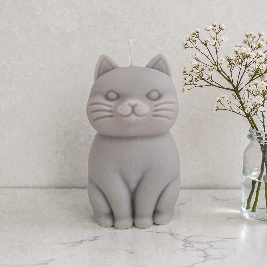 Sculptural cat-shaped soy pillar candle styled on marble surface with floral vase flowers and an open book in the background.
