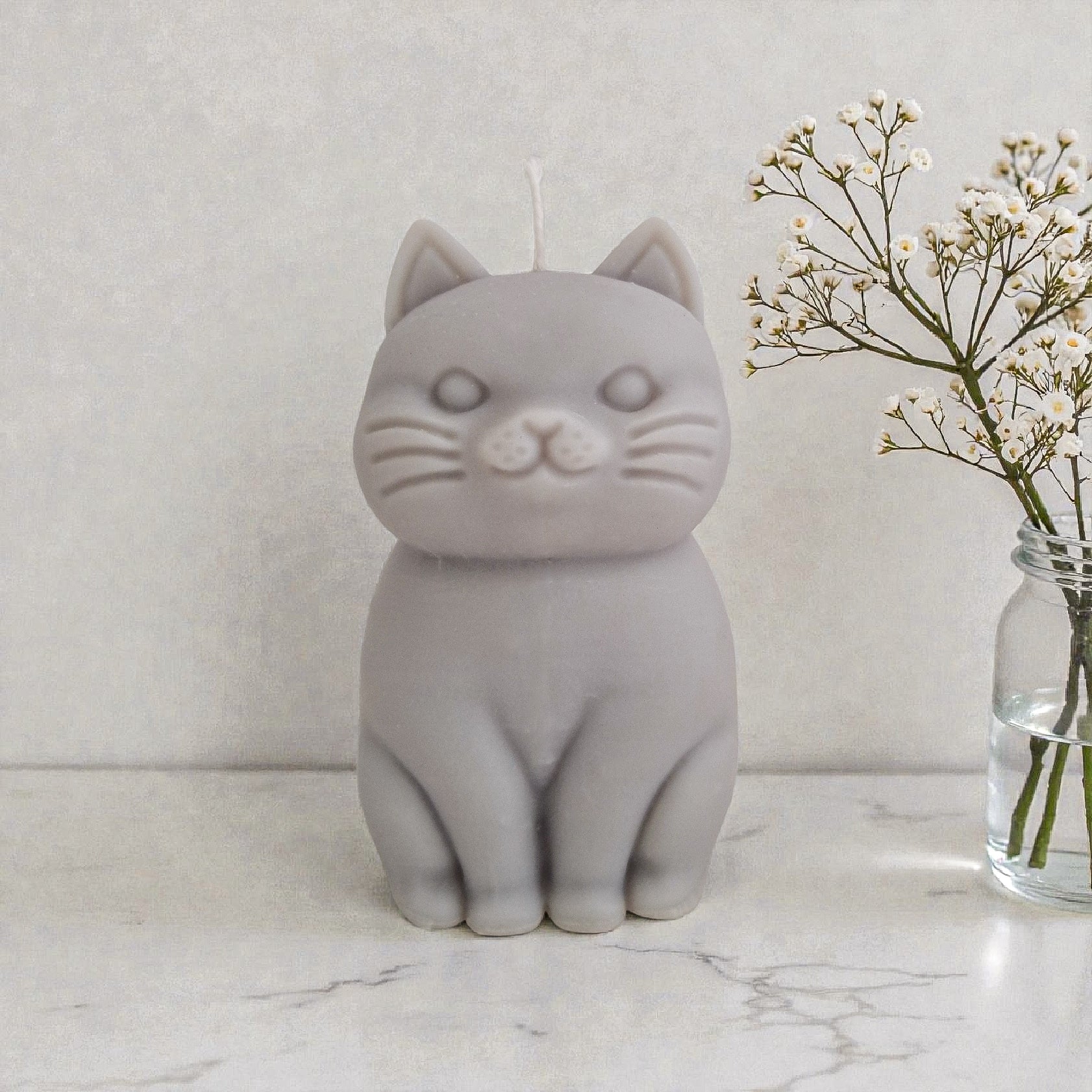 Sculptural cat-shaped soy pillar candle styled on marble surface with floral vase flowers and an open book in the background.