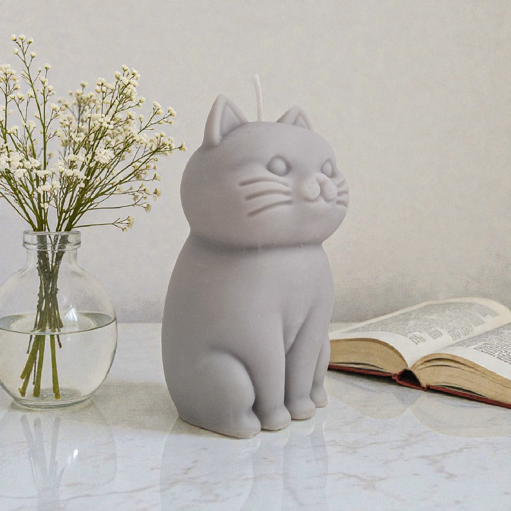 Sculptural cat-shaped soy pillar candle styled on marble surface with floral vase flowers and an open book in the background.