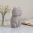 Sculptural cat-shaped soy pillar candle styled on marble surface with floral vase flowers and an open book in the background.
