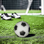 Classic black and white soy-wax candle soccer ball on a green field with goal post in the background and soccer shoes