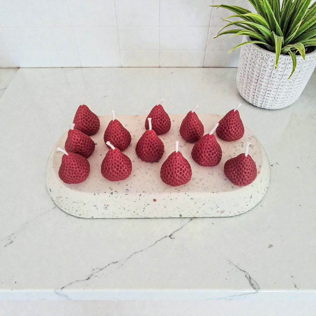 Red berry candles on a white stone surface with a plant in the background