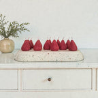 Decorative display of red pear-shaped candles on a speckled stone base with a plant in the background.