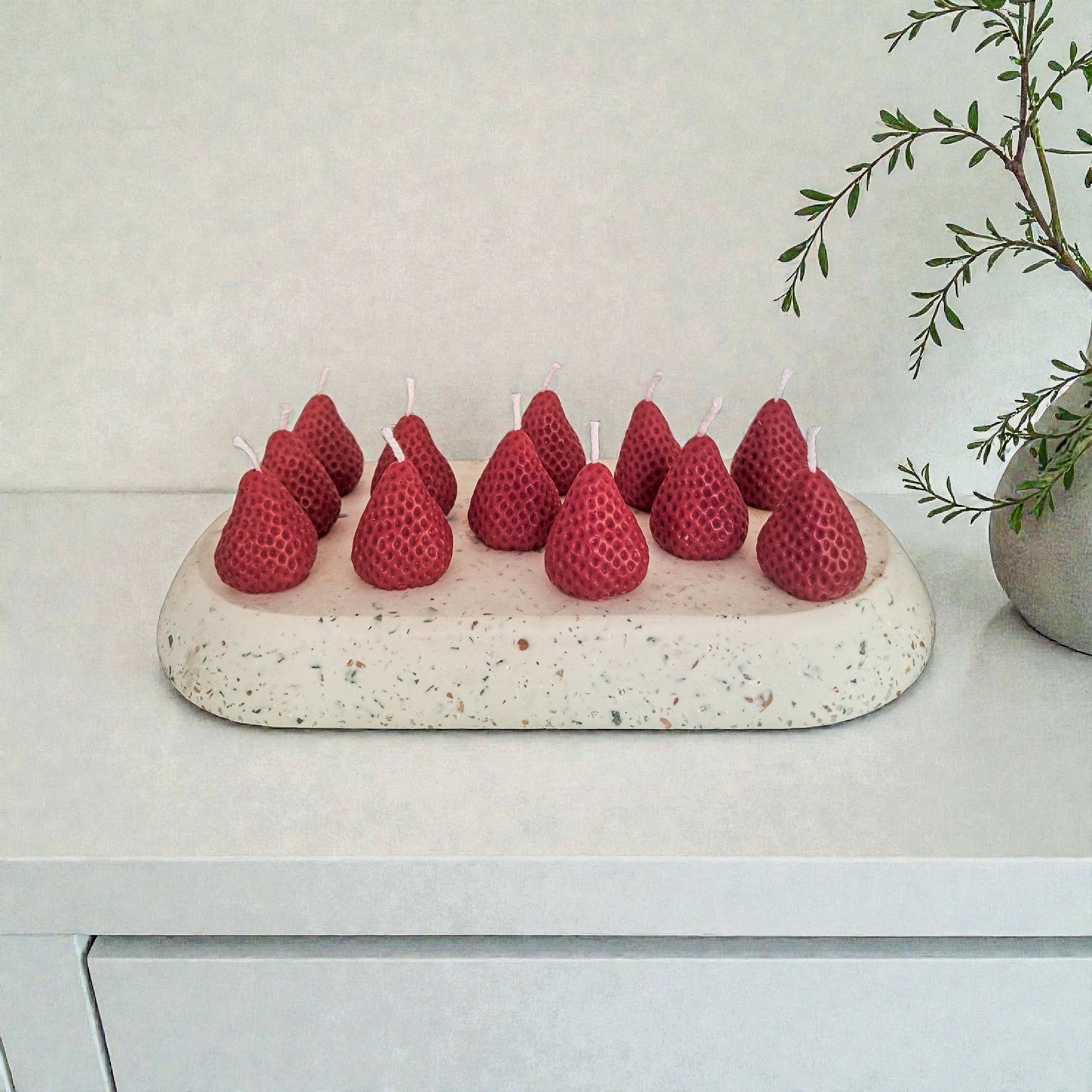 Red berry-shaped candles on a speckled stone holder with a plant in the background.