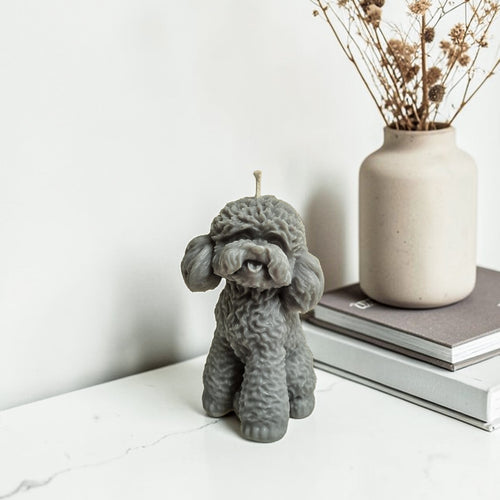 Gray dog-shaped soy wax candle on a white surface with a vase and books in the background