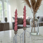 Hand poured soy wax pink spiral candles in silver holders on a marble surface with a blurred indoor background